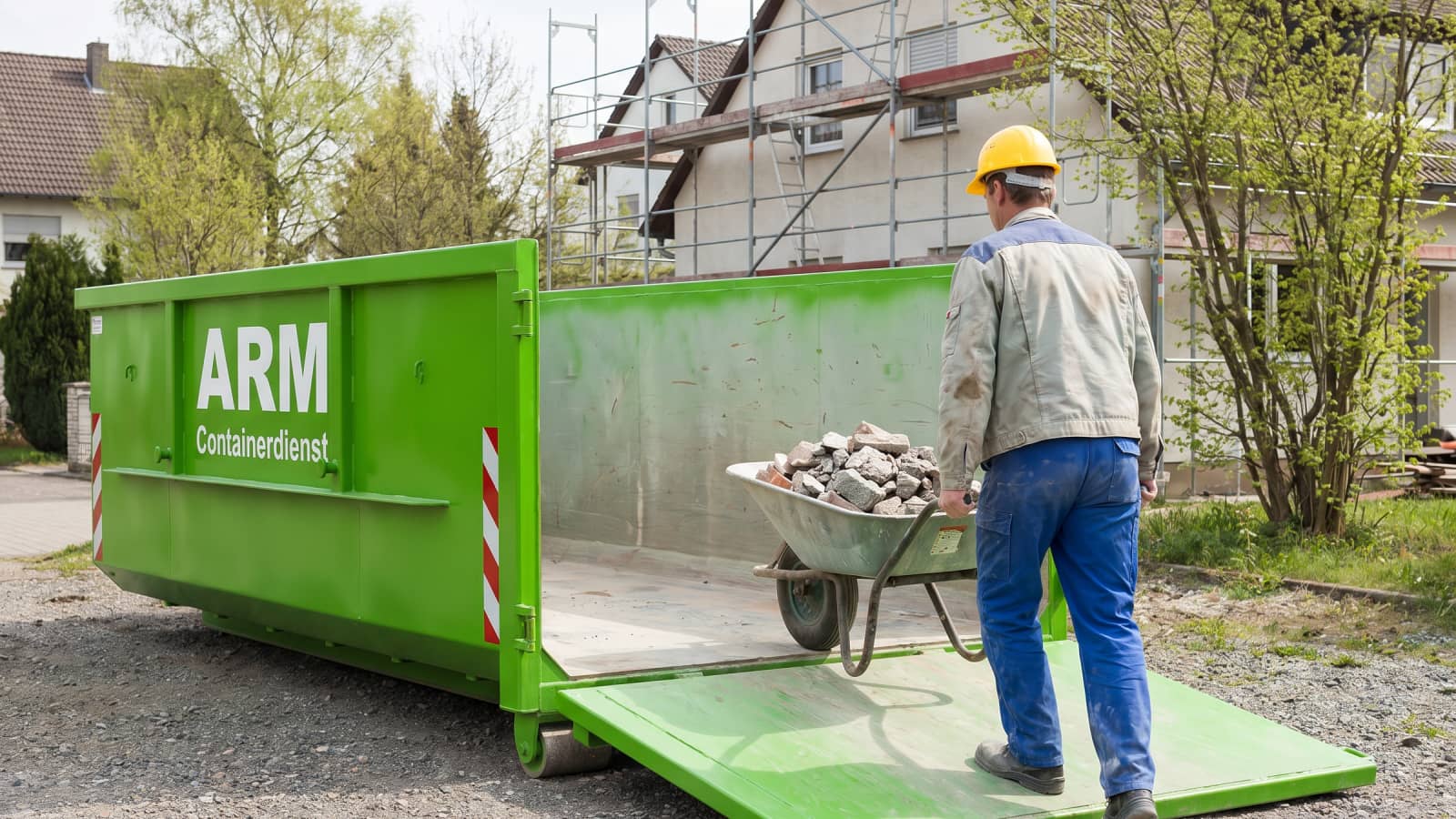 Arbeiter belädt grünen ARM-Container über die Klappe mit einer Schubkarre voll Bauschutt Arbeiter belädt grünen ARM-Container über die Klappe mit einer Schubkarre voll Bauschutt