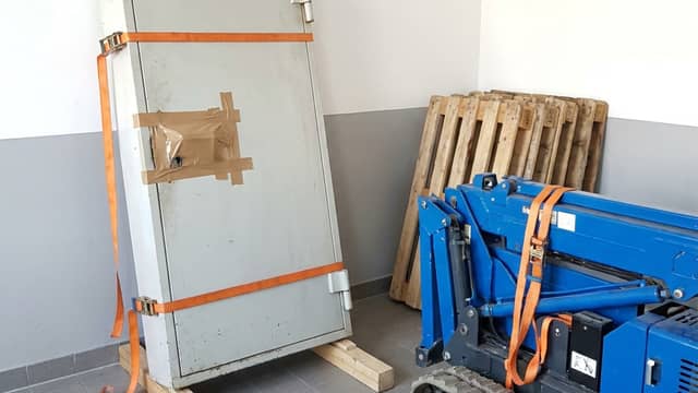 Ausgebaute Tresorraumtür steht mit Spanngurten gesichert auf Kanthölzern, daneben ein Raupenlift