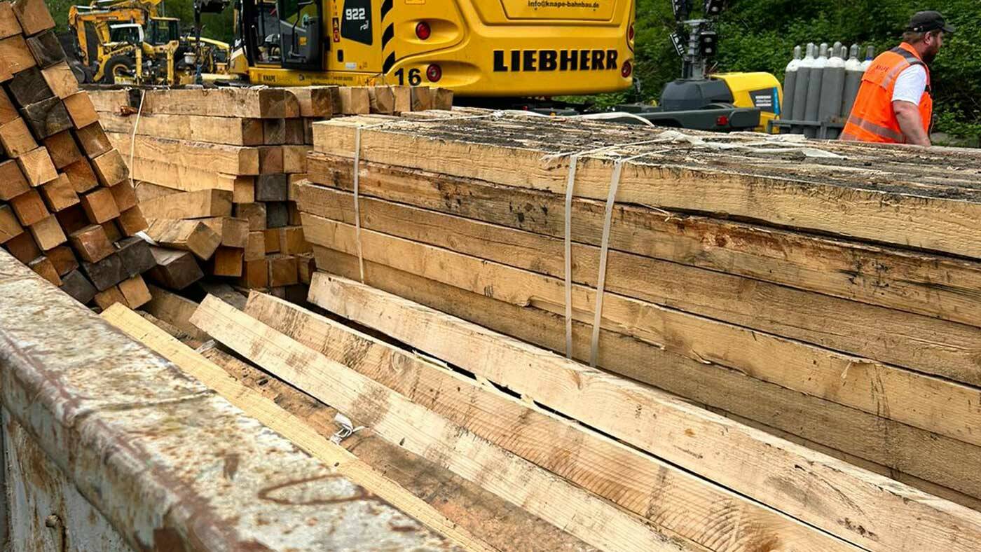 Alte, ausgetauschte Holzschwellen, gestapelt neben einem Container von "Containerdienst Frankfurt", bereit zur fachgerechten Entsorgung.